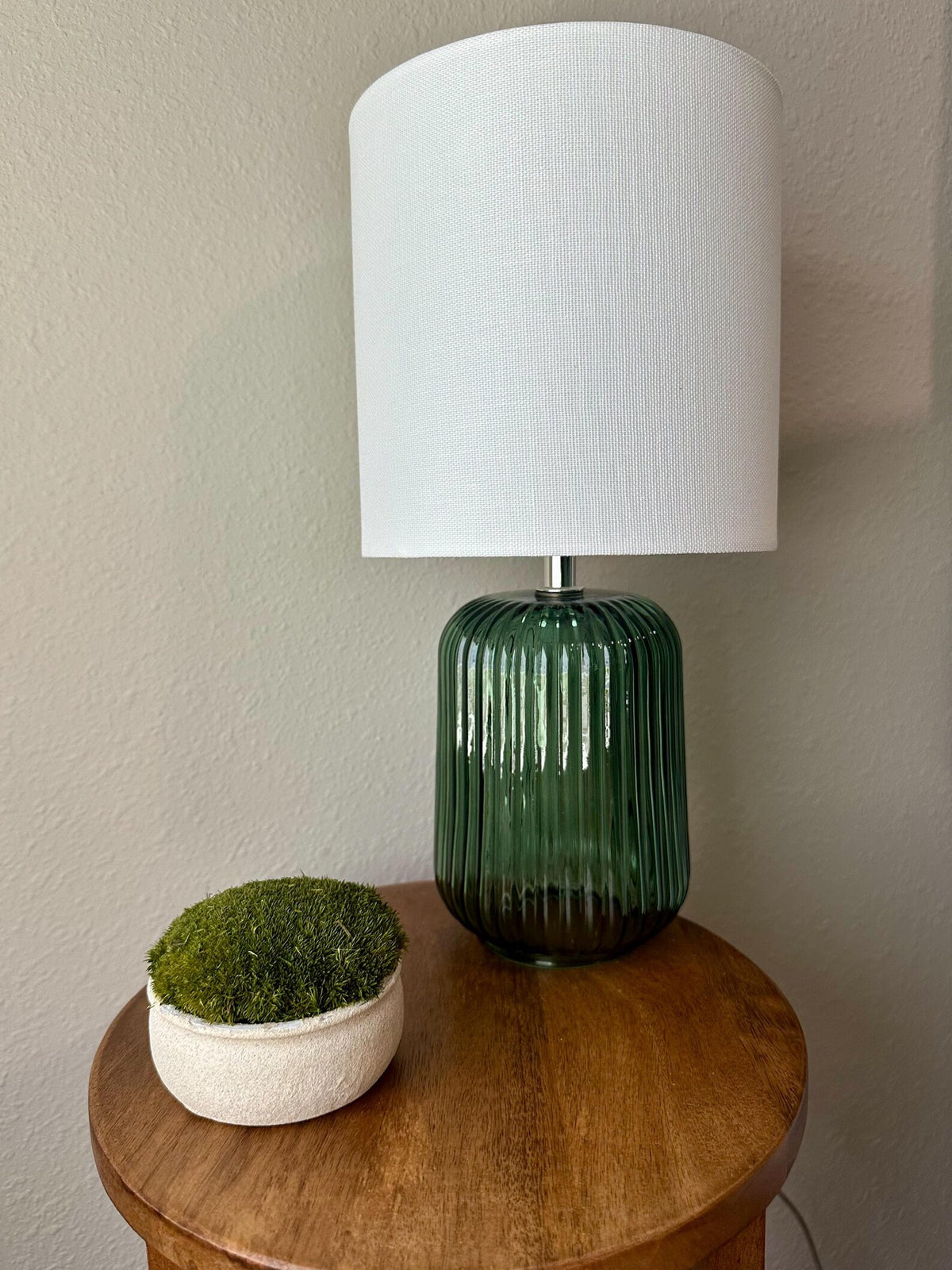 Mini upcycled beige textured bowl with dark green preserved moss styled on a wooden side table beside a lamp.