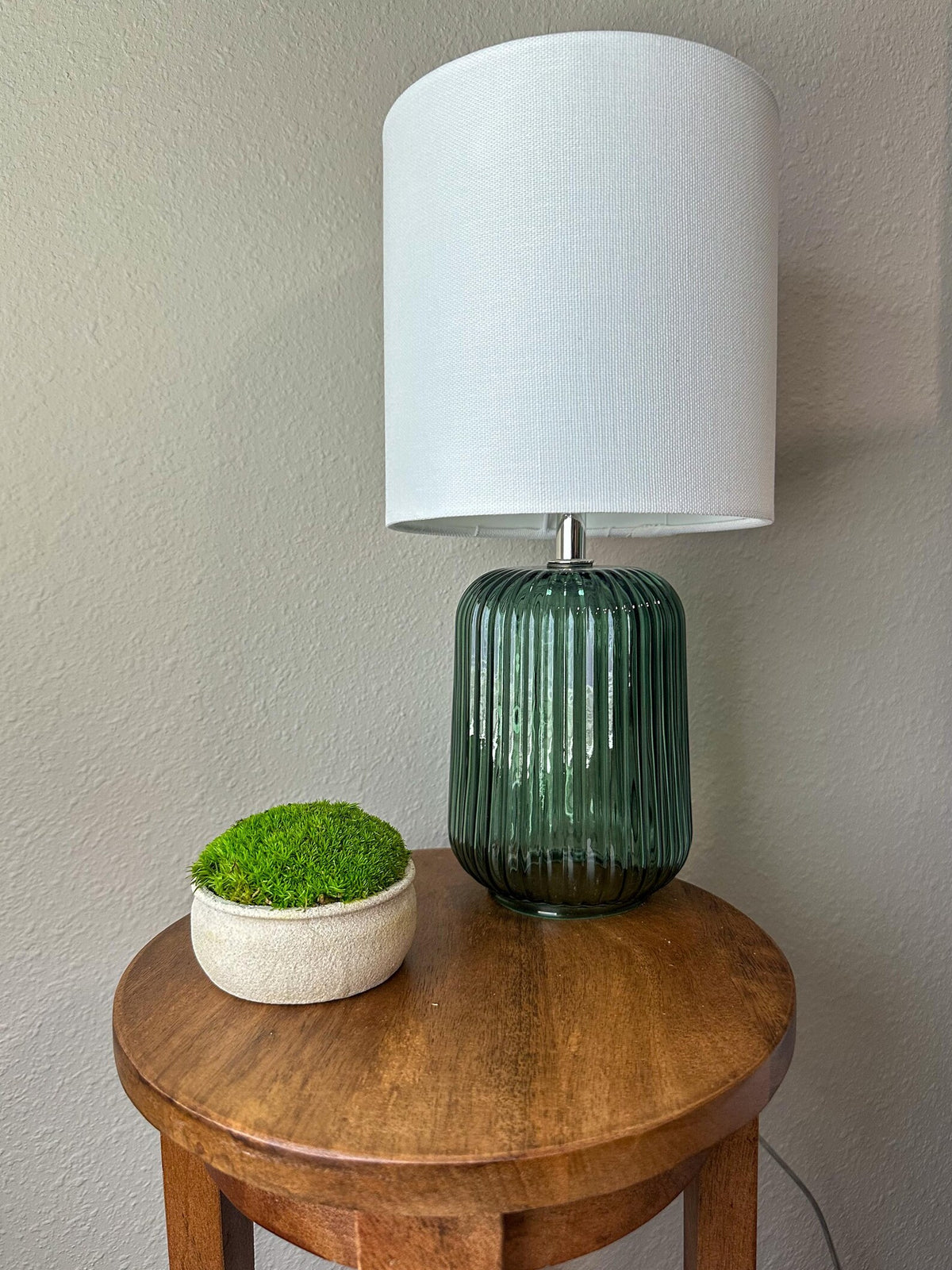 Mini upcycled beige textured bowl with light green preserved moss styled on a wooden side table beside a lamp.