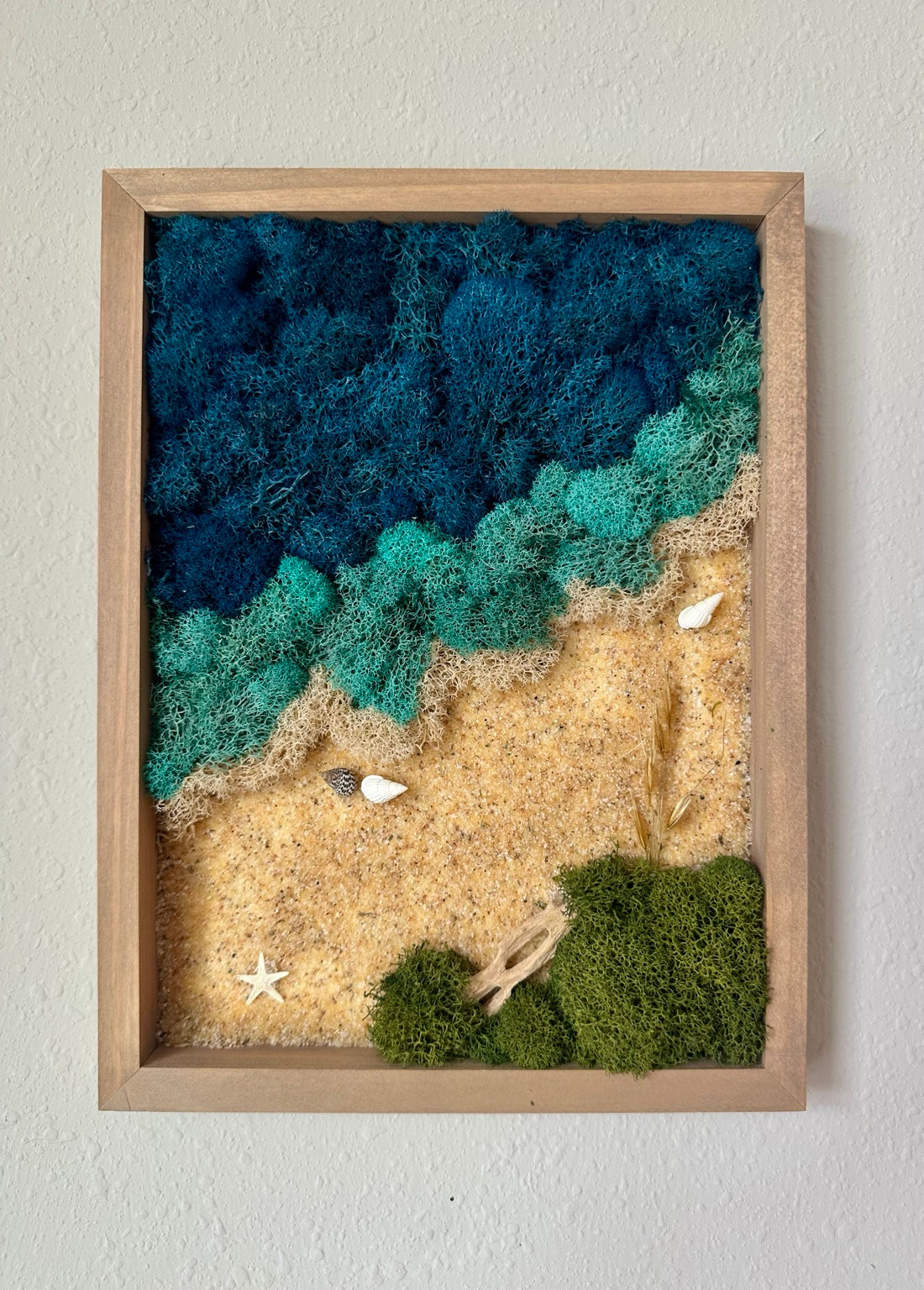 Vertical wood-framed beach scene with deep blue and turquoise preserved moss waves along a diagonal ivory shoreline, sand, shells, a starfish, green moss, and wood accents.